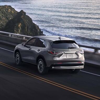 2027 Honda HR-V EX-L in Modern Steel Metallic rear view driving on a coastal road near the ocean (Subcompact Crossover SUV).